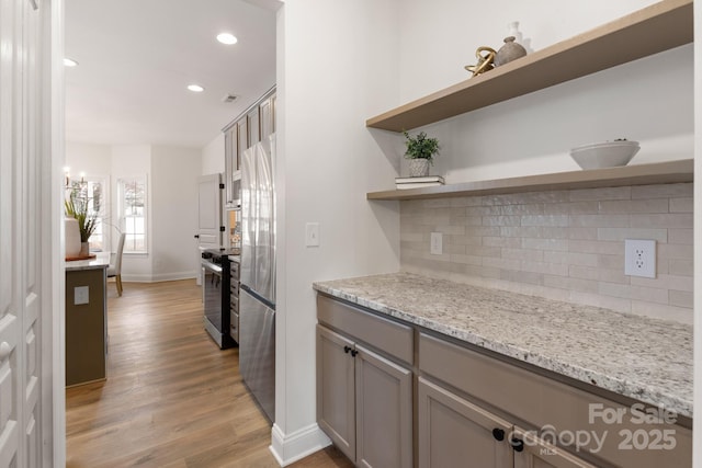 kitchen with light stone countertops, decorative backsplash, stainless steel appliances, gray cabinets, and light hardwood / wood-style floors