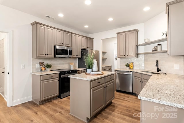 kitchen with gray cabinetry, stainless steel appliances, sink, a center island, and light hardwood / wood-style floors