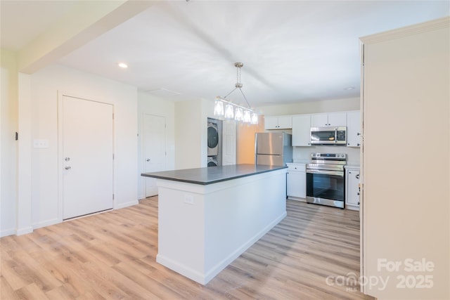 kitchen featuring appliances with stainless steel finishes, a kitchen island, decorative light fixtures, stacked washer and dryer, and white cabinetry