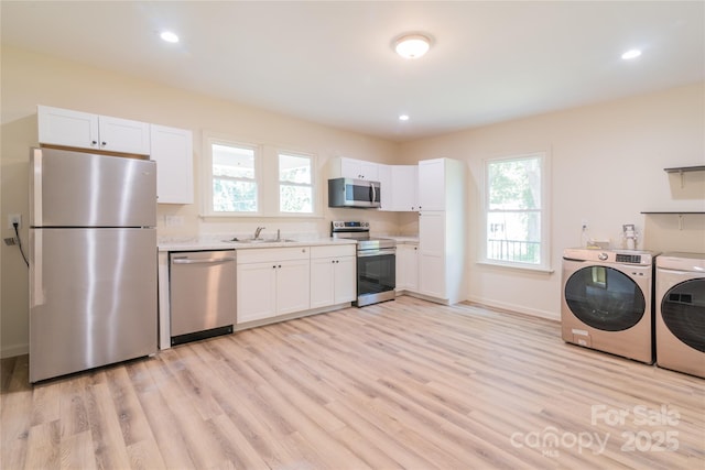 kitchen featuring white cabinets, washer and dryer, light wood-type flooring, and stainless steel appliances