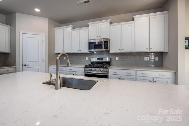 kitchen featuring stainless steel appliances, light stone countertops, decorative backsplash, white cabinets, and sink