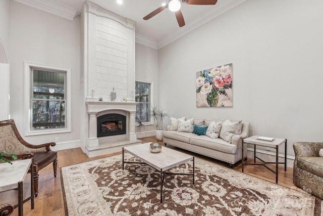 living room featuring ceiling fan, a large fireplace, hardwood / wood-style floors, a towering ceiling, and ornamental molding