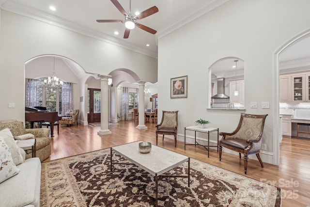 living room featuring ceiling fan with notable chandelier, light hardwood / wood-style floors, ornate columns, and ornamental molding