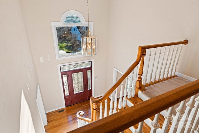 foyer entrance with wood-type flooring, a towering ceiling, and a notable chandelier