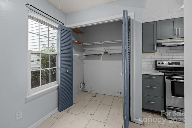 kitchen with stainless steel electric stove, gray cabinetry, and backsplash