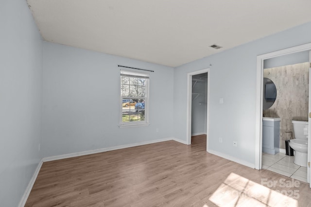 unfurnished bedroom featuring ensuite bathroom, a spacious closet, a closet, and light hardwood / wood-style floors