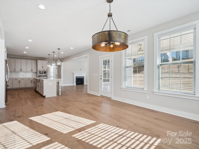 kitchen with stainless steel appliances, decorative light fixtures, decorative backsplash, a center island with sink, and light wood-type flooring