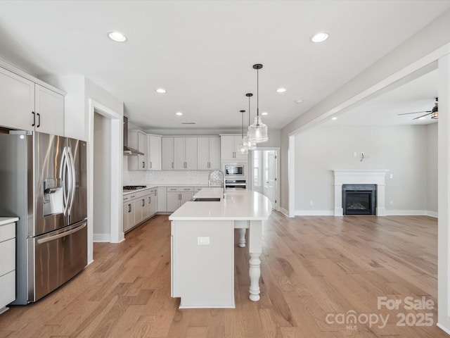 kitchen featuring white cabinetry, light hardwood / wood-style flooring, backsplash, a kitchen island with sink, and appliances with stainless steel finishes