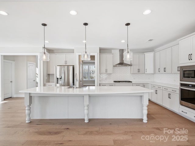 kitchen with wall chimney range hood, sink, an island with sink, white cabinetry, and stainless steel appliances