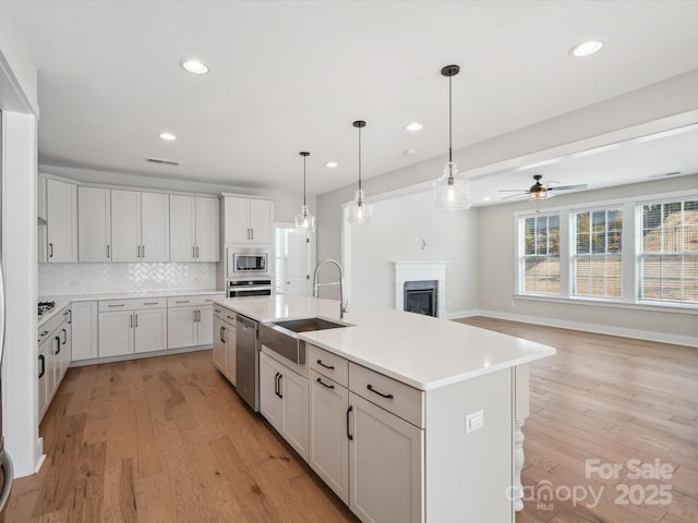 kitchen featuring sink, tasteful backsplash, an island with sink, white cabinets, and appliances with stainless steel finishes