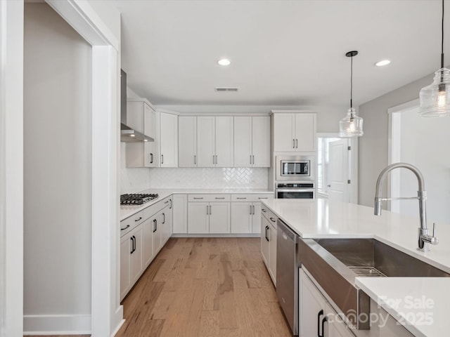 kitchen with sink, hanging light fixtures, stainless steel appliances, light hardwood / wood-style flooring, and white cabinets