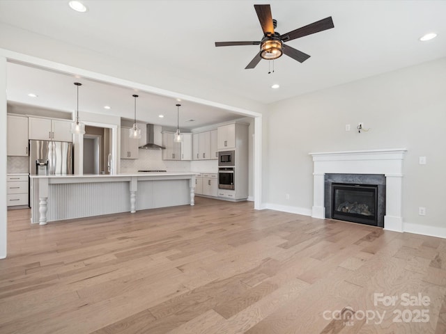 unfurnished living room with a fireplace, light wood-type flooring, ceiling fan, and sink