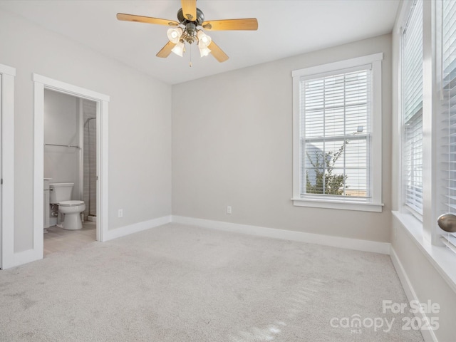 unfurnished bedroom with ceiling fan, light colored carpet, connected bathroom, and multiple windows