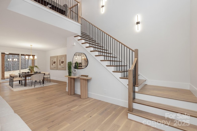 staircase with a chandelier, a towering ceiling, baseboards, and wood finished floors