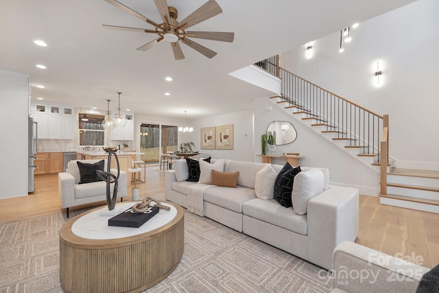 living area featuring recessed lighting, stairway, light wood-type flooring, baseboards, and ceiling fan with notable chandelier