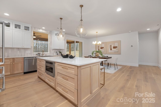 kitchen with light countertops, decorative backsplash, appliances with stainless steel finishes, light wood-style floors, and a kitchen island