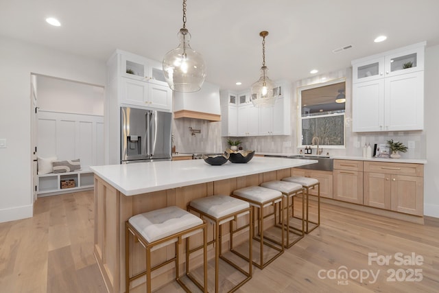 kitchen featuring visible vents, a kitchen island, a sink, light wood-type flooring, and stainless steel fridge