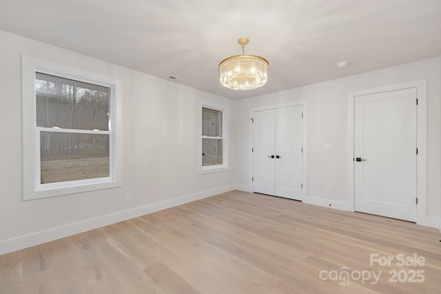 unfurnished room with an inviting chandelier, light wood-style flooring, and baseboards