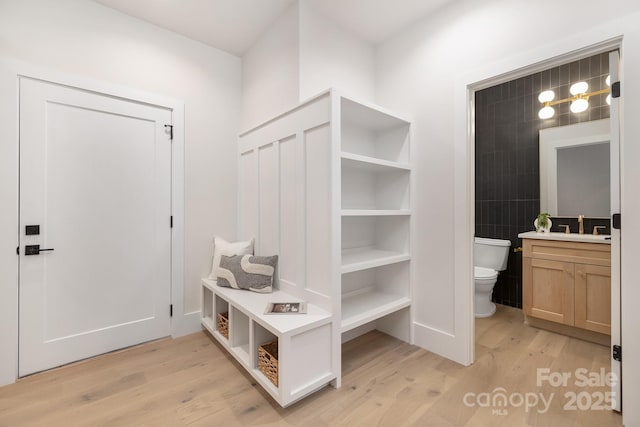 mudroom with light wood-type flooring, a sink, and tile walls