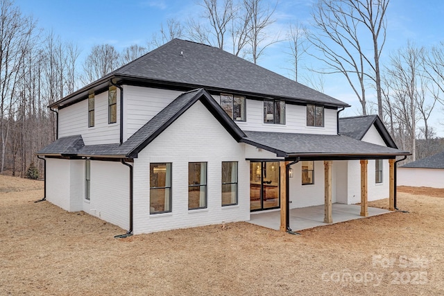 rear view of property with a shingled roof, a patio, and brick siding