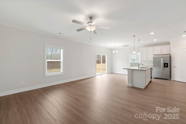 kitchen featuring stainless steel refrigerator with ice dispenser, decorative light fixtures, a center island with sink, white cabinets, and ceiling fan with notable chandelier