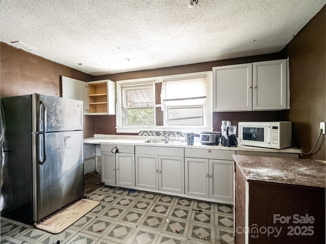 kitchen featuring stainless steel refrigerator, white cabinetry, and sink