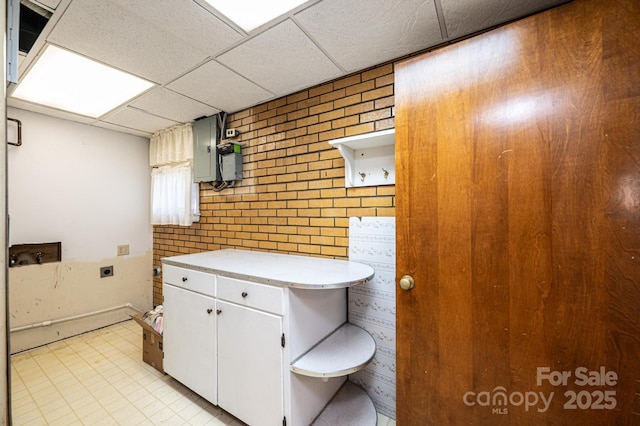 bathroom with electric panel, a drop ceiling, and brick wall