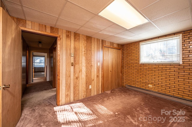 carpeted spare room with brick wall, a paneled ceiling, a baseboard heating unit, and wood walls