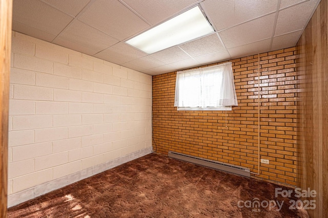 carpeted spare room with a paneled ceiling, baseboard heating, and brick wall