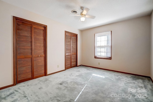 unfurnished bedroom with ceiling fan, multiple closets, and carpet