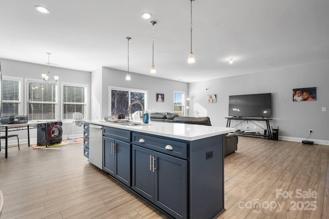 kitchen featuring sink, hanging light fixtures, light wood-type flooring, an island with sink, and blue cabinetry