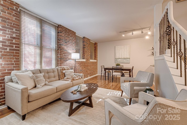 living room with rail lighting, brick wall, and light wood-type flooring