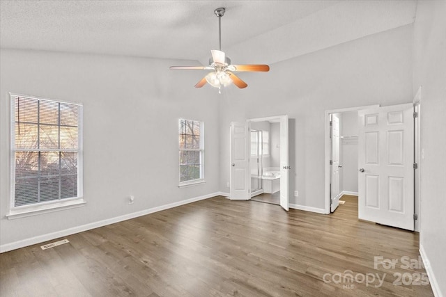 unfurnished bedroom with ensuite bathroom, ceiling fan, a spacious closet, and dark wood-type flooring