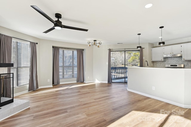 unfurnished living room with light wood-type flooring, a healthy amount of sunlight, and ceiling fan with notable chandelier