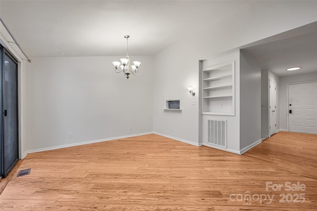 unfurnished room featuring light hardwood / wood-style floors, a chandelier, and built in shelves