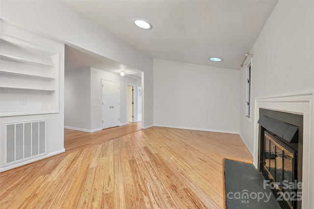 unfurnished living room with built in shelves and light hardwood / wood-style flooring