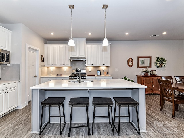 kitchen with sink, white cabinets, hardwood / wood-style floors, an island with sink, and hanging light fixtures