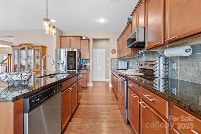 kitchen with stainless steel appliances, dark stone countertops, sink, backsplash, and a center island with sink