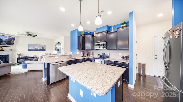 kitchen with appliances with stainless steel finishes, backsplash, a kitchen island, and hanging light fixtures