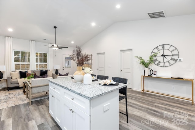 kitchen with light stone countertops, white cabinets, a center island, a kitchen bar, and hardwood / wood-style flooring