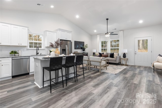 kitchen with ceiling fan, a kitchen island, stainless steel appliances, white cabinets, and light stone counters