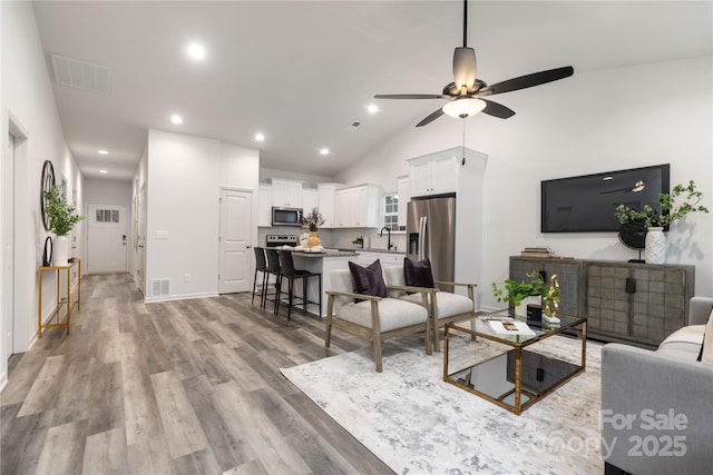 living room featuring ceiling fan, sink, vaulted ceiling, and light wood-type flooring