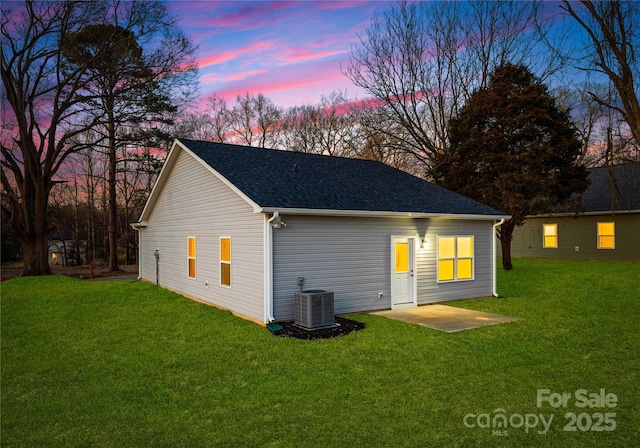 back house at dusk featuring a yard, a patio, and central AC unit