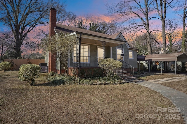 property exterior at dusk with a carport, a yard, and covered porch