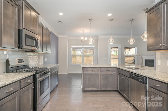 kitchen featuring hanging light fixtures, sink, appliances with stainless steel finishes, dark brown cabinets, and light stone counters