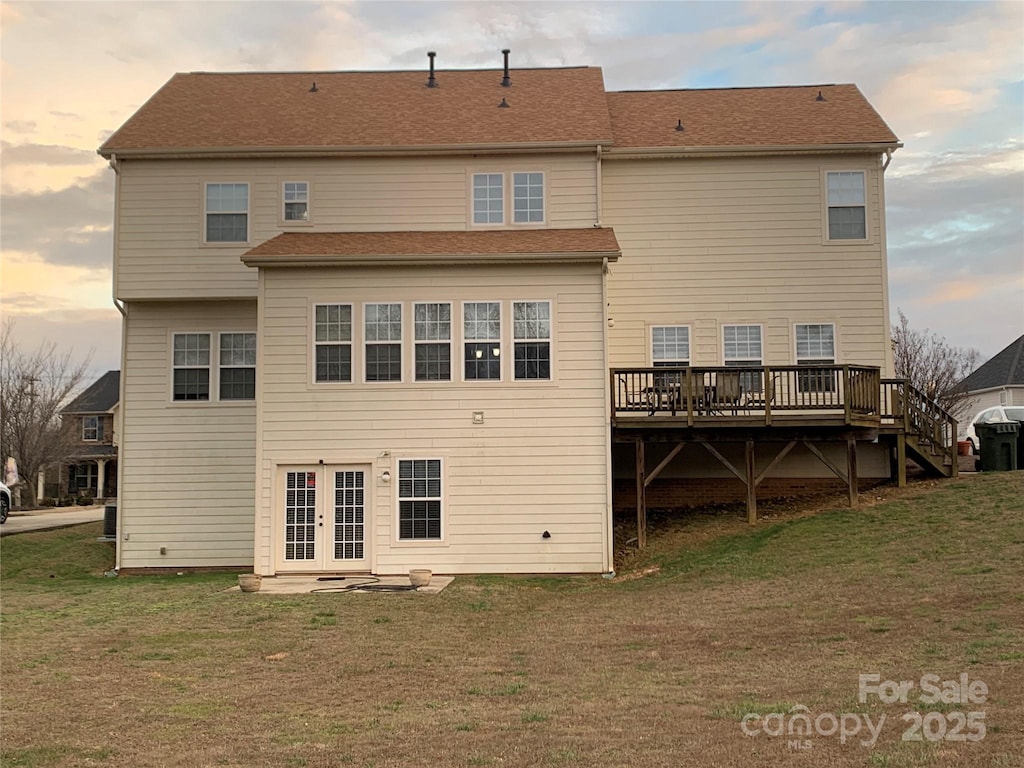 back house at dusk with a lawn, a wooden deck, and french doors