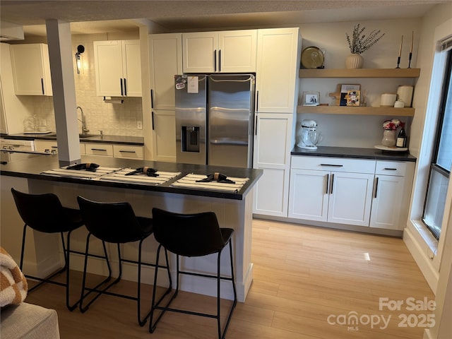 kitchen featuring a kitchen bar, stainless steel fridge, white cabinets, and light hardwood / wood-style floors