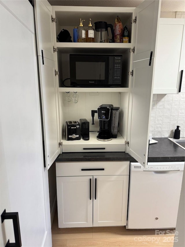 bar featuring backsplash, white cabinetry, dishwasher, and light wood-type flooring