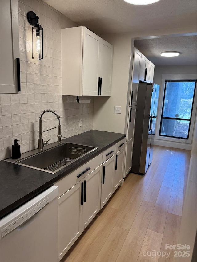 kitchen featuring stainless steel refrigerator, white cabinetry, dishwasher, sink, and light hardwood / wood-style flooring