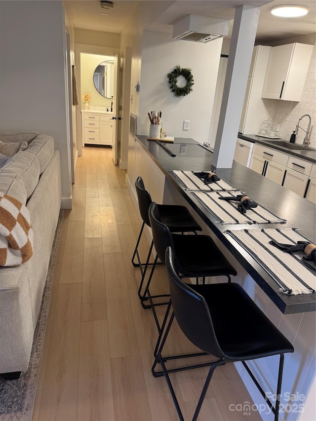 kitchen featuring white cabinets, sink, light hardwood / wood-style flooring, tasteful backsplash, and a breakfast bar area